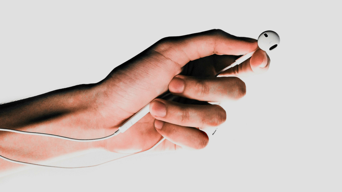 Eine Hand hält Kopfhörer in der Hand – ein Symbol für die wachsende Rolle von KI am Mikrofon und die Zukunft digitaler Audioinhalte.